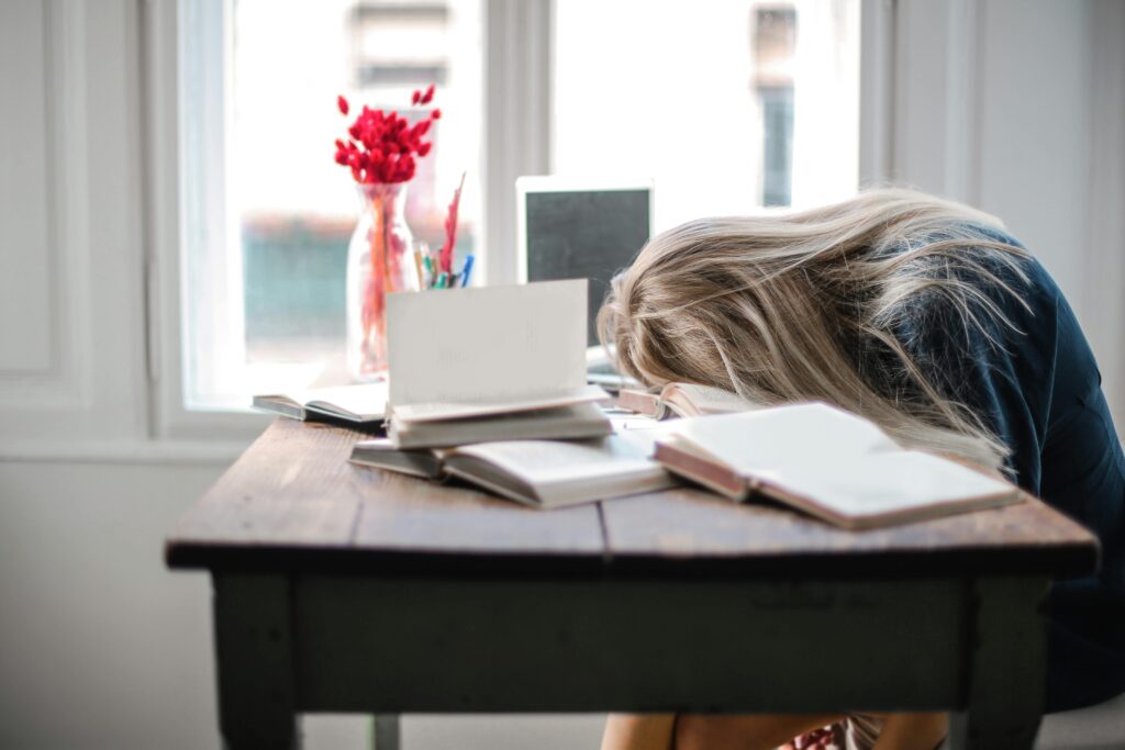 pexels photo 3767411 3767411 Blonde woman slumped over desk filled with books, showcasing study fatigue indoors.